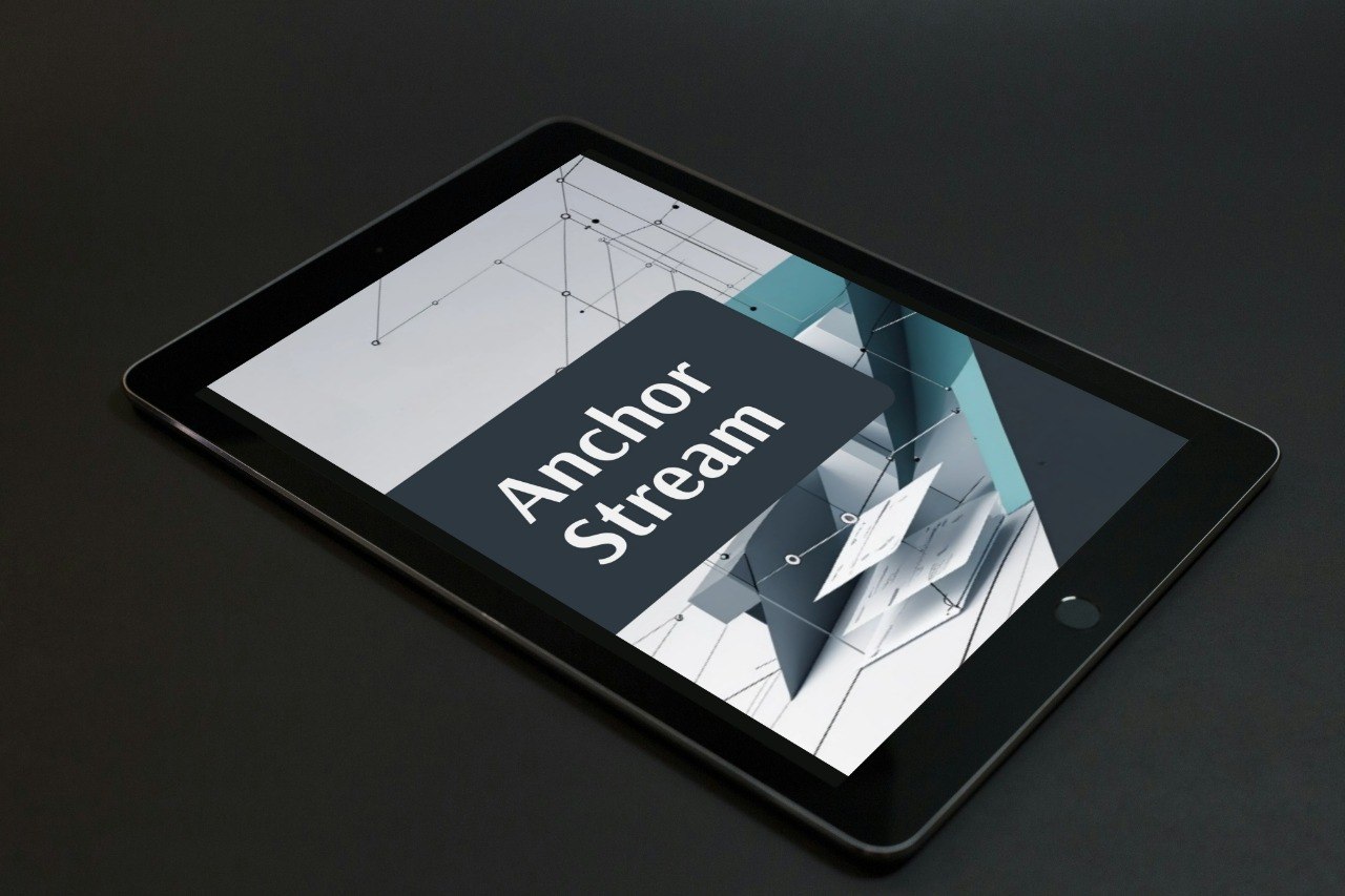 A black tablet device shown at an angle on a dark surface, displaying a digital cover with the text 'Anchor Stream' over a geometric abstract graphic.