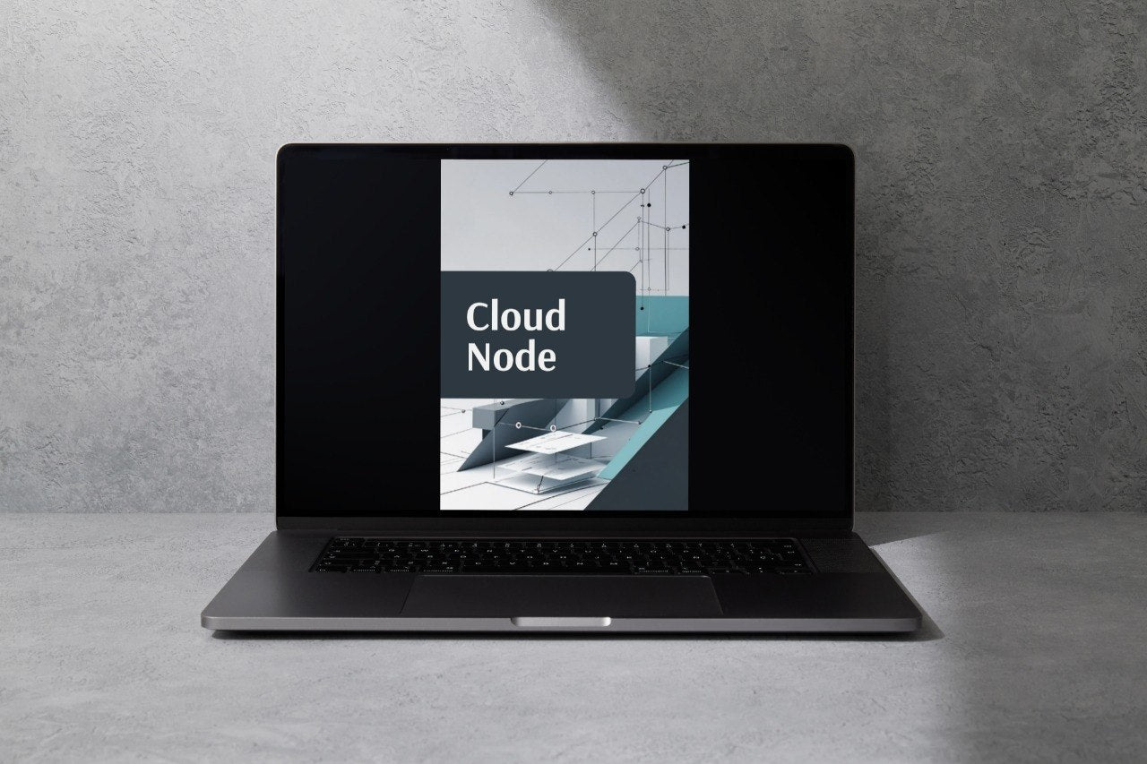 A dark gray laptop sits open on a light gray surface against a textured gray wall, with the screen displaying the text 'Cloud Node' over a tech-themed graphic.