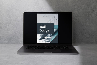 A dark gray open laptop sits on a light gray surface against a textured gray wall. The screen displays a graphic with the text 'Trail Design' over an architectural trail illustration.